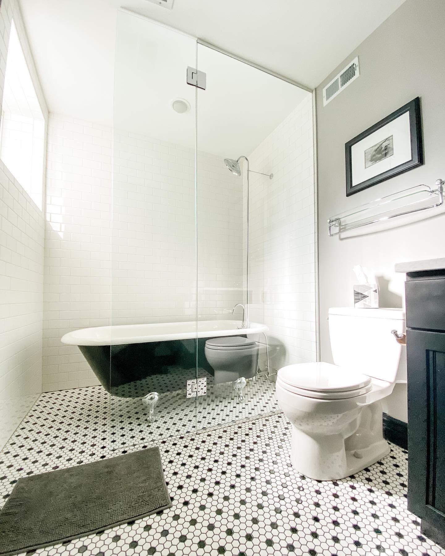 Contemporary bathroom with glass shower, clawfoot tub, and black-and-white tile flooring.